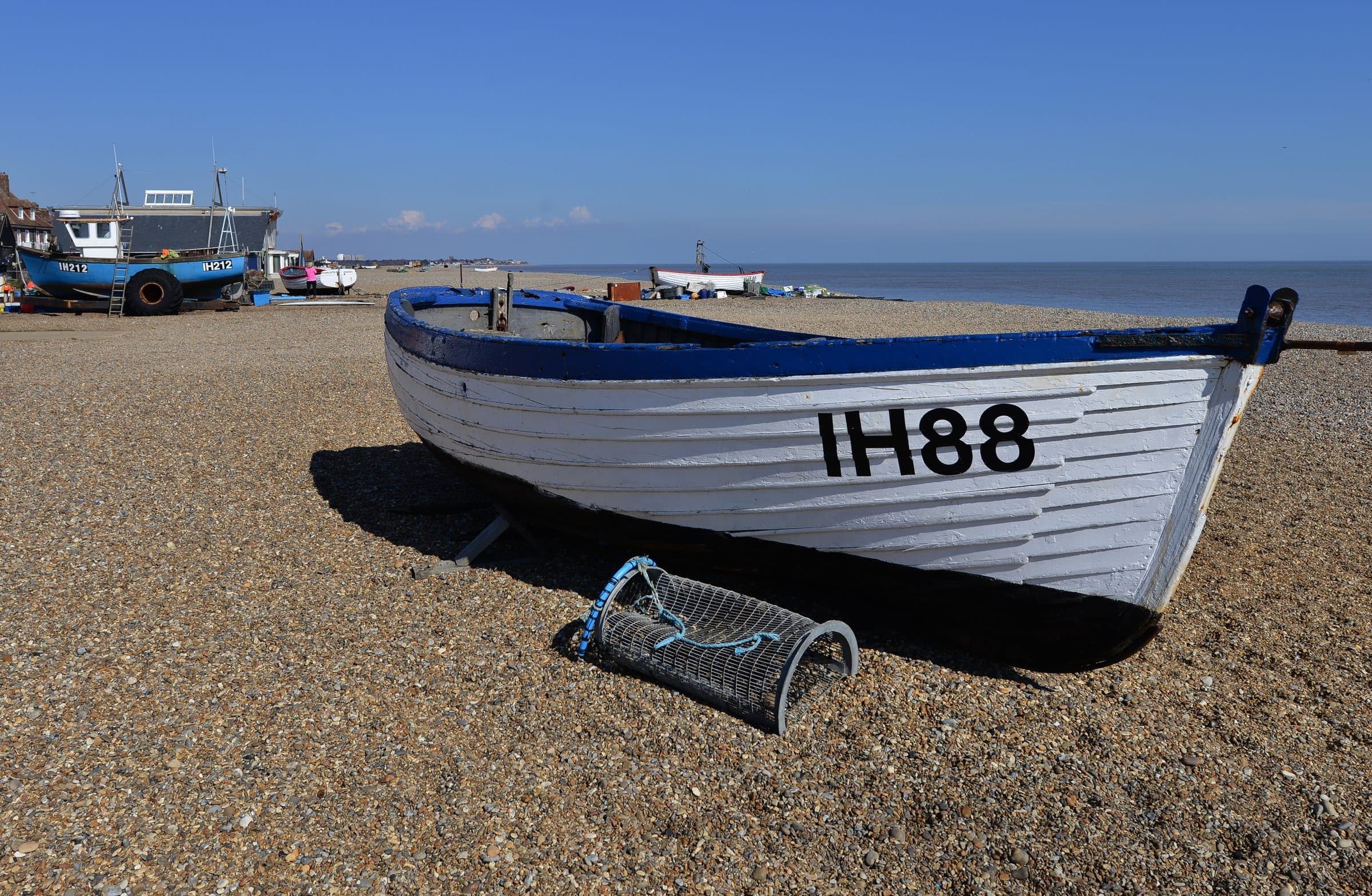 A blue and white clinker-built fishing boat marked IH88 hauled up on the shingle at Aldeburgh, with other boats and the North Sea behind.
