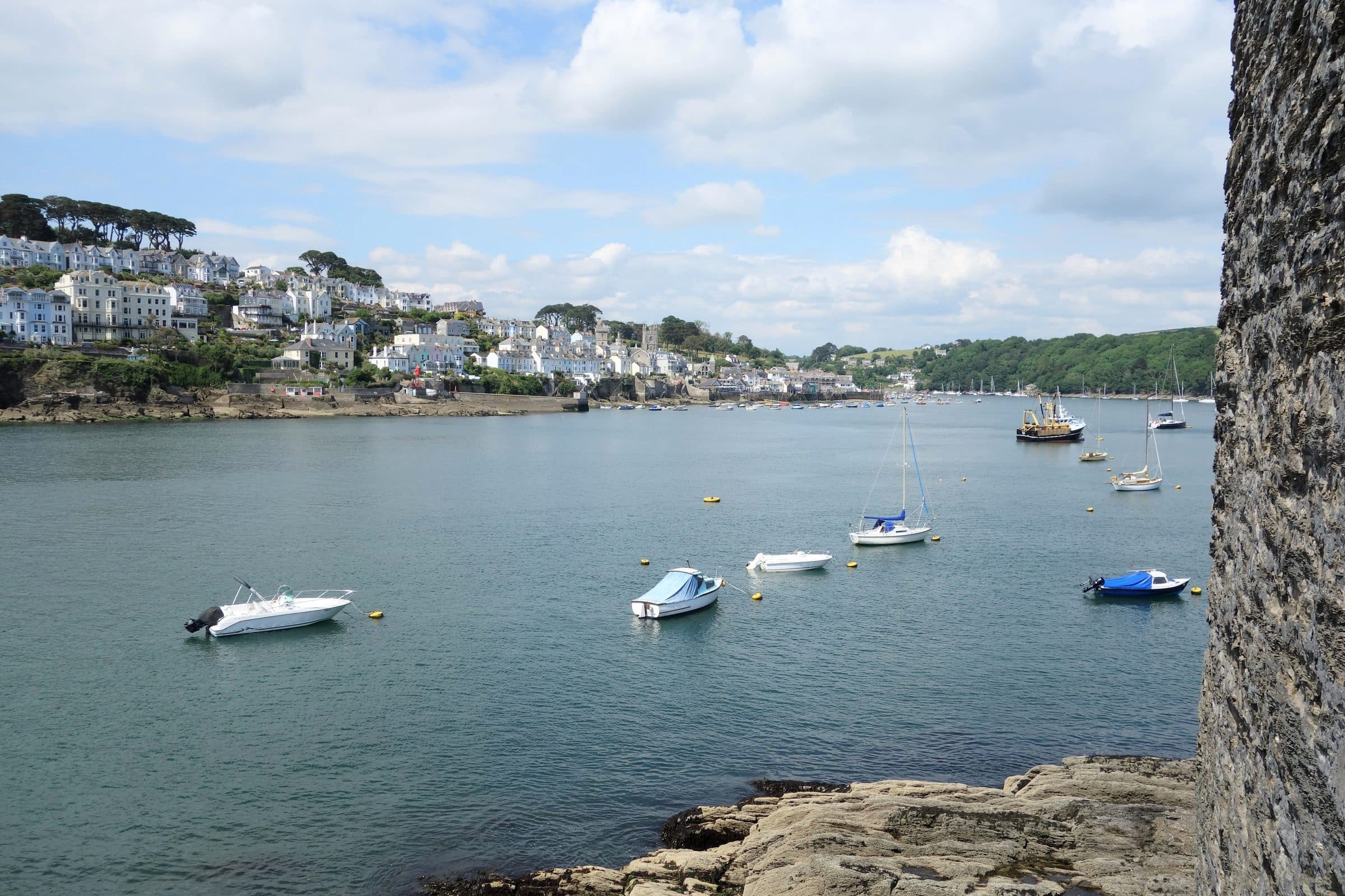 The Fowey estuary in Cornwall, with small boats moored on green water and the town rising up the far bank.