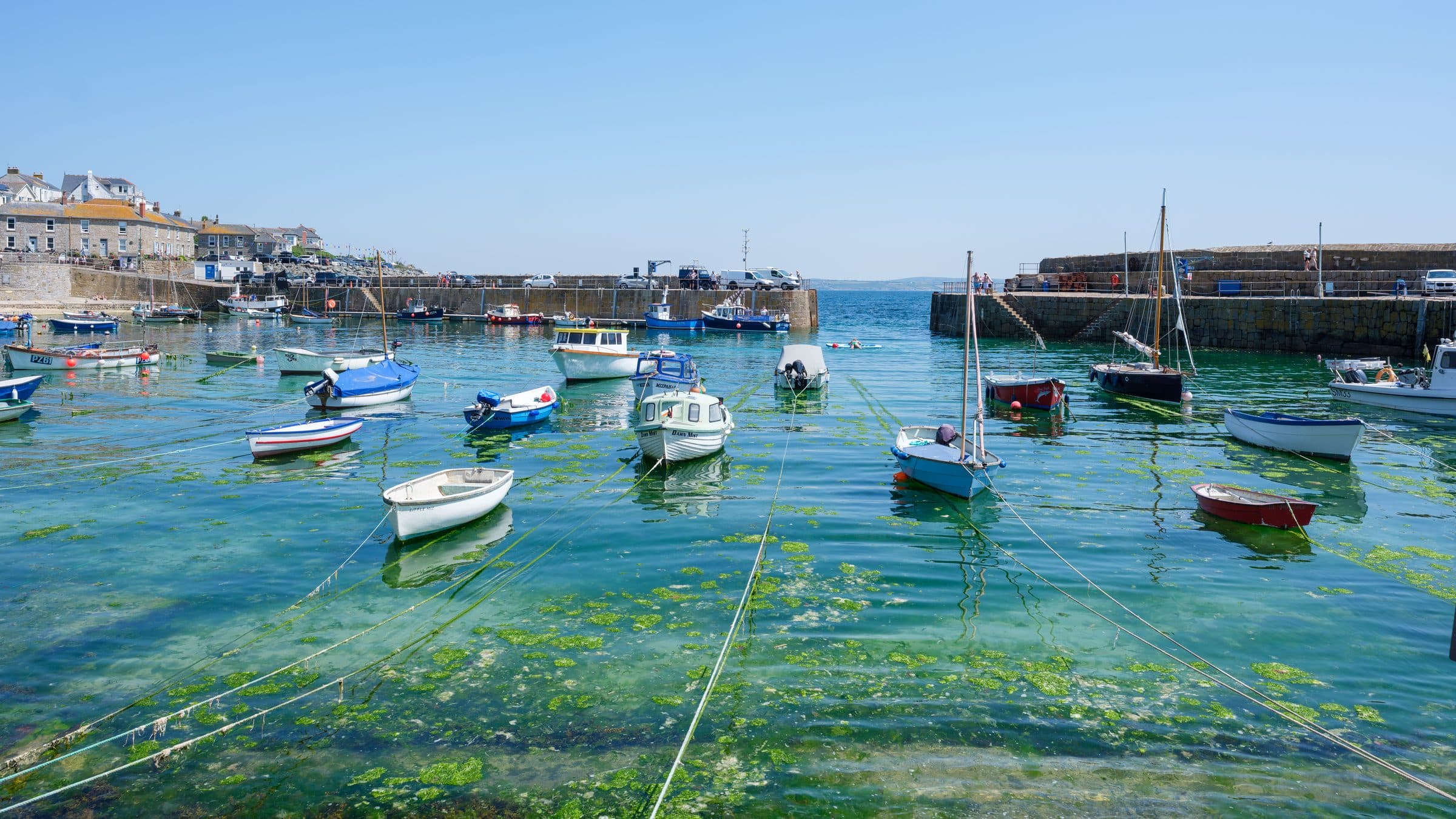 Small boats moored in the sheltered harbour at Mousehole in Cornwall, with the granite harbour walls and village behind.