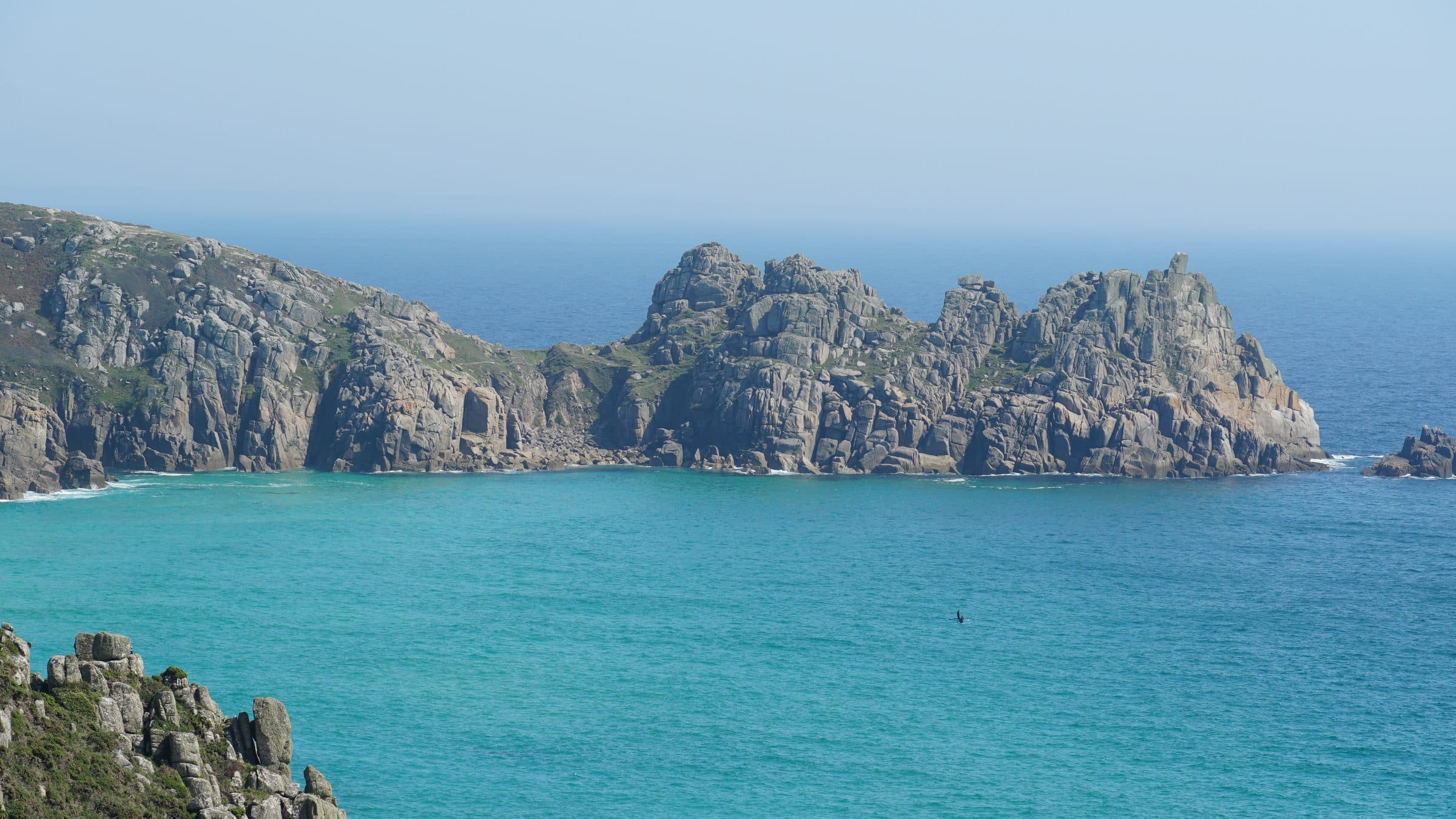 The granite headland and Logan Rock above the turquoise water at Porthcurno in Cornwall.