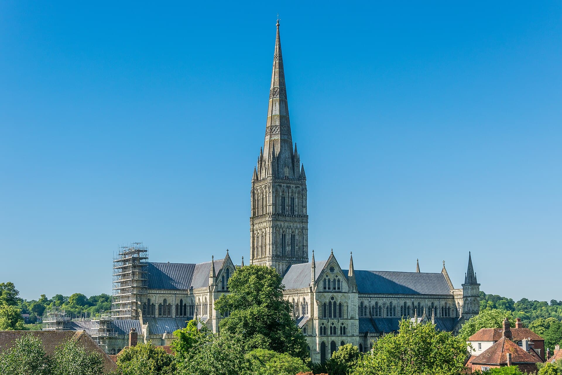 The spire of Salisbury Cathedral rising above the trees, the tallest in Britain, seen against a clear summer sky.