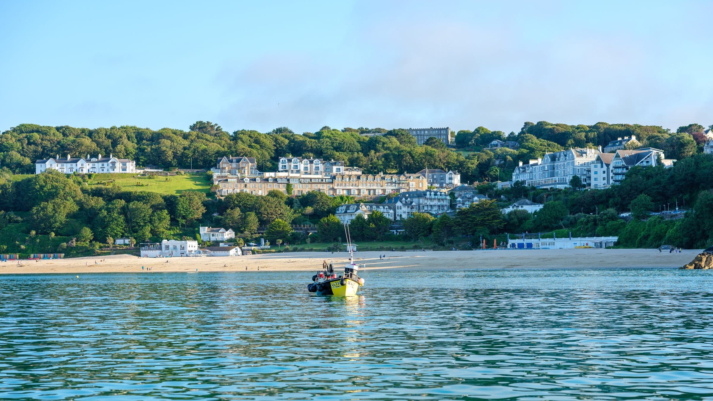 St Ives seen from the water, Porthminster beach and the town rising above a turquoise sea with a small boat in the foreground.