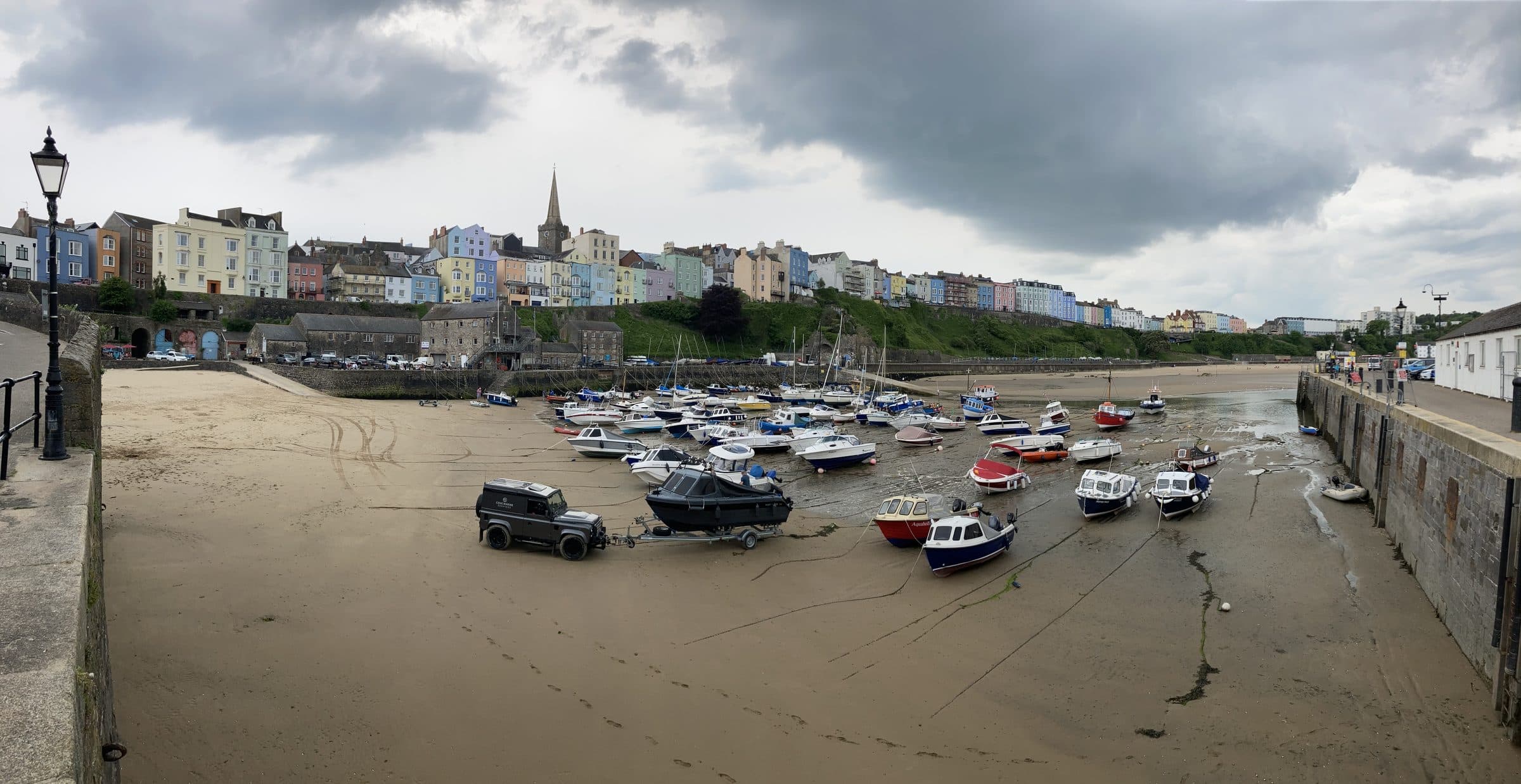 Tenby harbour at low tide, boats resting on the sand below the town's pastel-painted houses and church spire.