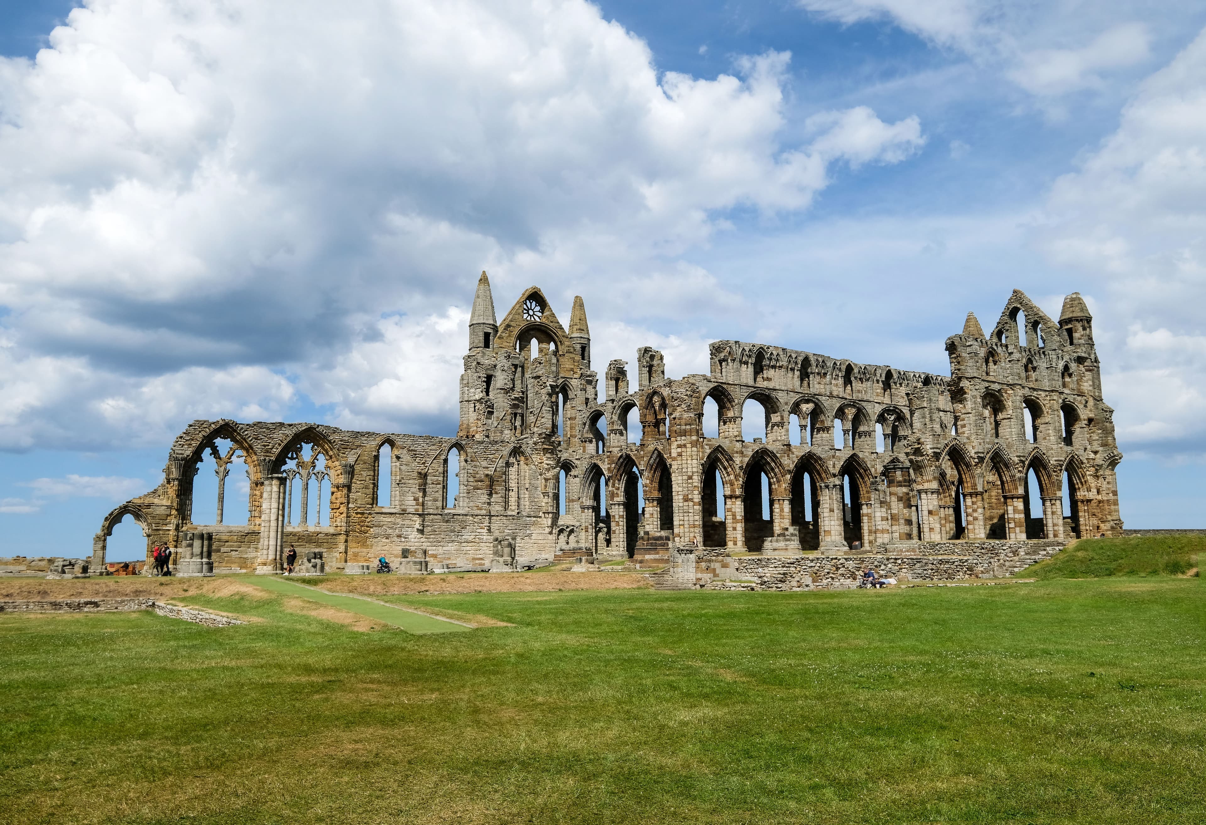 The ruins of Whitby Abbey standing on the headland above the town, its empty Gothic arches against a cloudy sky.